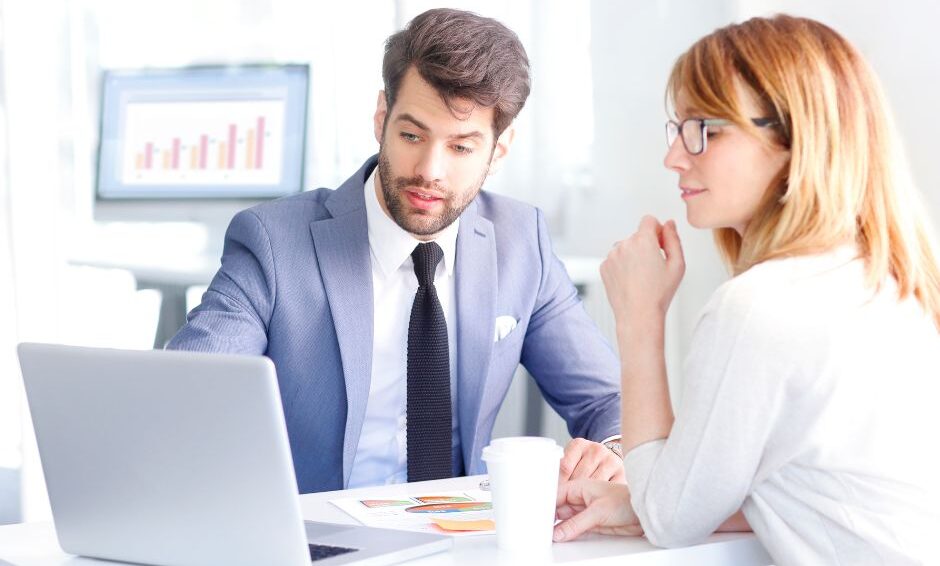 man showing something to a woman on a computer in a light office space
