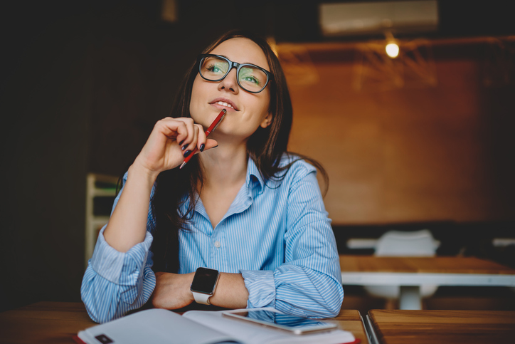 Dreamy woman podring while working on journalistic publication sitting with notebook in cafe,thoughtful female student in eyewear doing homework task solving problems and analyzing information woman analyzing HR-data