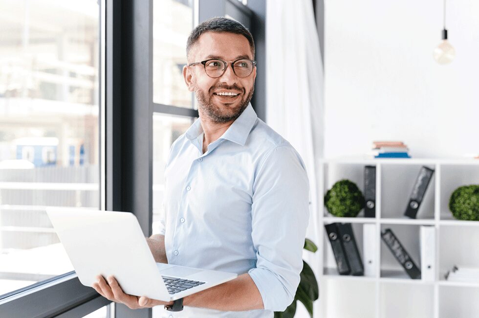 Man smiling in an office holding a laptop